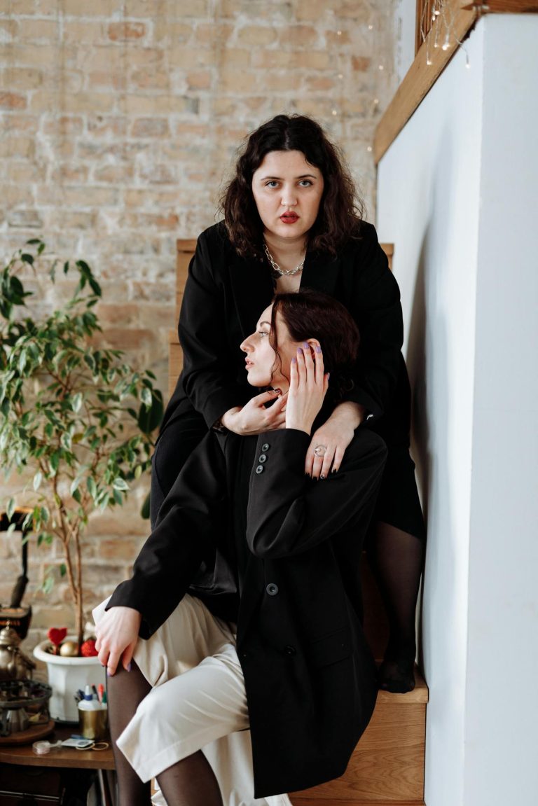 A fashionable couple in black attire shares a moment indoors, exuding elegance and intimacy.