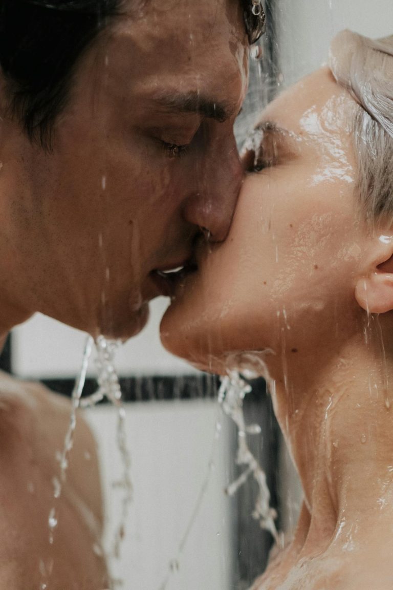A passionate couple shares an intimate kiss while showering together.