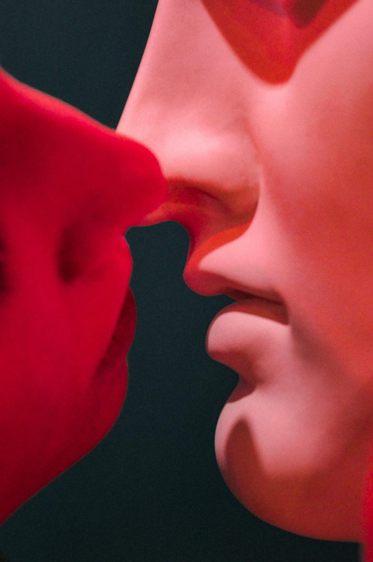 Close-up of a sculpture kiss under red light, evoking romance and passion.