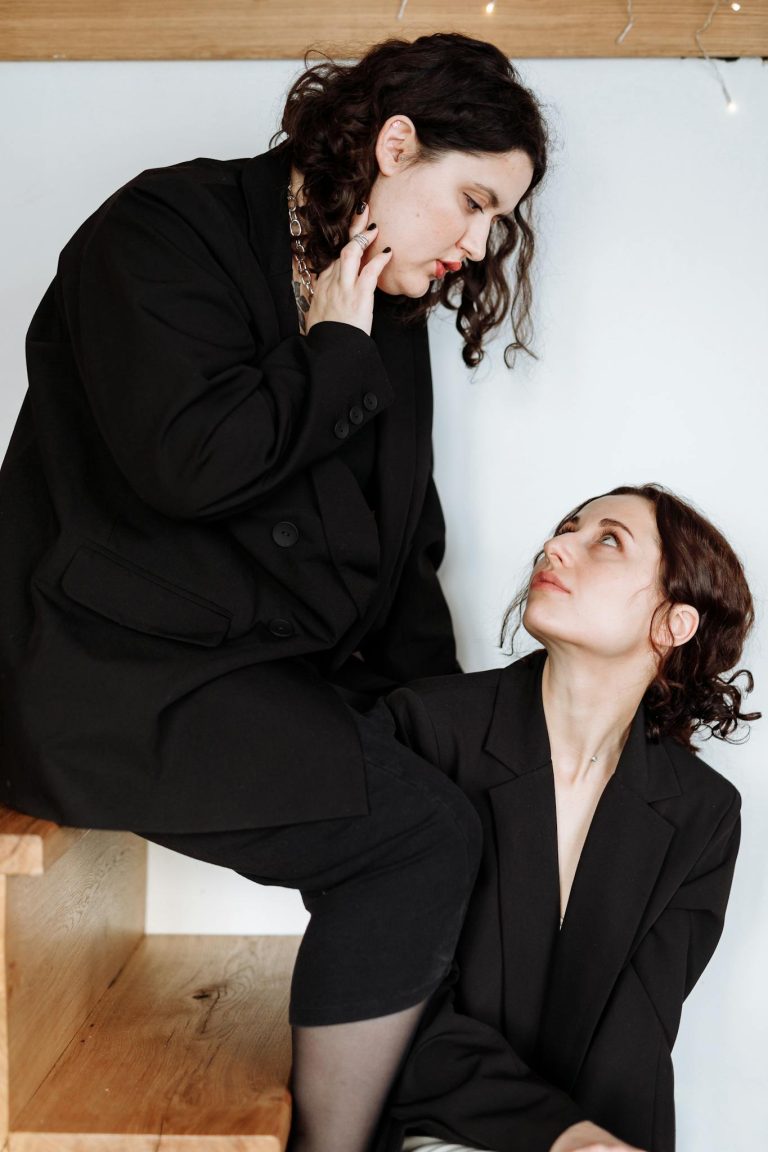 Two women sharing an intimate and thoughtful moment indoors, dressed in contemporary fashion.